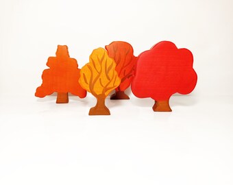 May include: Four wooden tree figurines in shades of orange and red. The trees have brown trunks and varying leaf shapes, with one featuring a yellow and orange color scheme. The background is white.