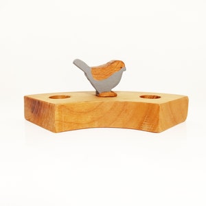 May include: A wooden birdhouse with two holes and a gray wooden bird perched on top.