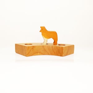May include: A wooden toy with a small wooden animal figure standing on top. The animal is a light brown color and has a white chest. The base of the toy is a light brown color and has three holes in it.