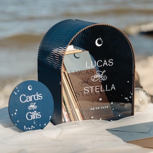 May include: A navy blue wedding card box with the names "Lucas and Stella" and the date "08-08-2028" printed on it. A matching round sign that says "Cards and Gifts" is also present. The scene is set on a beach.