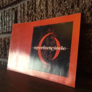 May include: A red sticker with a black and white logo of a circle with the text "a perfect circle" in white.