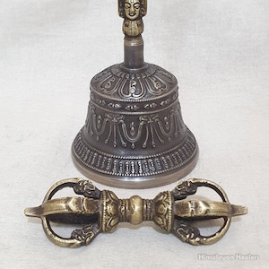 May include: A traditional Tibetan Buddhist ritual bell and dorje, or vajra, made of brass. The bell has a detailed design with a deity face on the handle. The dorje has a double-headed design.