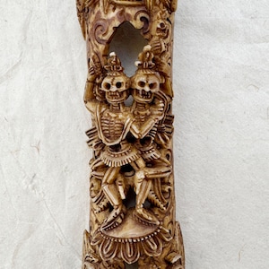 Peut inclure: Sculpture en bois sculpté représentant une tête de dragon, des squelettes et d'autres figures. La sculpture est de couleur marron clair et présente des sculptures complexes. Le texte "Himalayan Healers" est en bas.