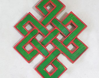 Op de afbeelding: Een groene houten knoop met een rode omtrek. De knoop is een traditioneel Tibetaans symbool dat bekend staat als de oneindige knoop, die eeuwigheid en onderlinge verbondenheid symboliseert.