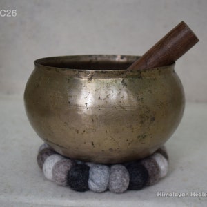 Peut inclure: Un grand bol chantant en laiton d'aspect antique avec un batteur en bois. Le bol repose sur un coussin en feutre gris et noir.