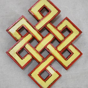 Puede incluir: Un nudo de madera amarillo y rojo, también conocido como nudo infinito tibetano, es un símbolo de buena suerte y eternidad. El nudo está intrincadamente tallado y pintado con un contorno rojo y un centro amarillo.
