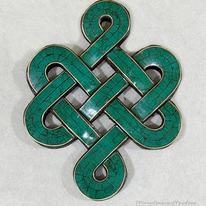 May include: A turquoise-colored Endless Knot pendant with a gold-colored border. The knot design is made of small, square-shaped pieces. The pendant is a symbol of interconnectedness and is often used in spiritual practices.