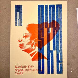Könnte beinhalten: Ein Vintage-Poster mit cremefarbenem Hintergrund zeigt ein Profil einer Person in Orange und eine blaue Herzform. Der Text "NINA SIMONE" ist in blauen vertikalen Blöcken gehalten. Zusätzlicher Text enthält das Datum "21. März 1969" und den Ort "Sophia Gardens Pavilion Cardiff".