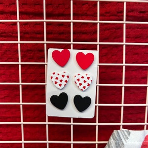 May include: A set of six heart-shaped earrings. Two are solid red, two are white with red polka dots, and two are solid black.