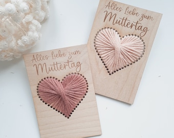 Puede incluir: Dos tarjetas de madera con el texto "Alles Liebe zum Muttertag" y un corazón de hilo rosa en cada tarjeta.