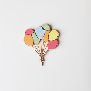 Könnte beinhalten: Ein hölzernes Ballongeschenk mit bunten Ballons in Rosa, Gelb, Orange, Grün und Blau. Die Ballons sind an dünnen Holzstäben befestigt, wodurch ein festliches Design entsteht. Ideal für Partydekorationen.