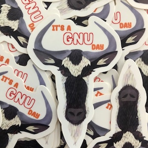 Peut inclure: Un lot d'autocollants représentant un gnou de dessin animé avec le texte "It's a GNU Day" en lettres orange. Les autocollants sont blancs avec un fond gris et ont une finition brillante.