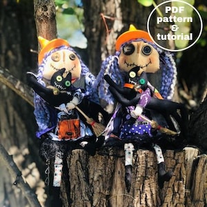 Op de afbeelding: Twee handgemaakte lappenpoppen gekleed als heksen met zwarte katten. De poppen dragen paarse en zwarte jurken met oranje hoeden en hebben zwart garenhaar. De poppen zitten op een boomstam.  PDF-patroon & tutorial.