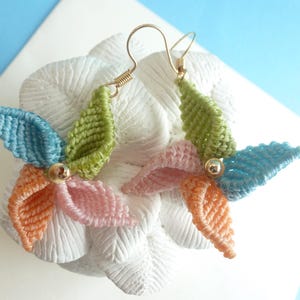May include: A pair of handmade earrings featuring a flower design with blue, green, pink, and orange crocheted petals. The earrings are made with gold-colored wire and have a small bead in the center of each flower.