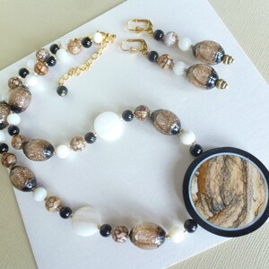 May include: A brown, black, and white glass bead necklace with a large round pendant. The pendant is made of brown, black, and white marbled glass. The necklace is paired with matching earrings.