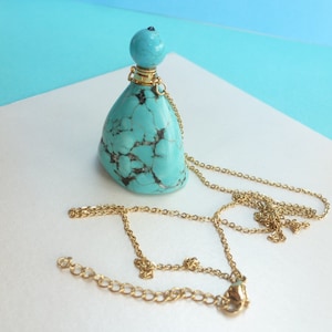 Peut inclure: Un collier avec un pendentif en forme de bouteille de couleur bleu turquoise. La bouteille est en pierre turquoise et a un bouchon doré. Le collier est fait d'une chaîne dorée.