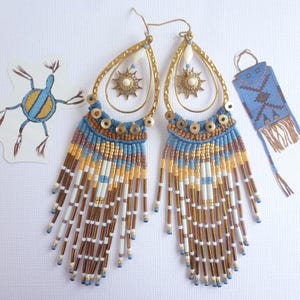 Könnte beinhalten: Ein Paar lange, geperlte Ohrringe mit einem goldenen Reifen und einem blauen und goldenen Quasten. Die Ohrringe sind aus verschiedenen Perlen gefertigt, darunter blaue, goldene, weiße und braune.
