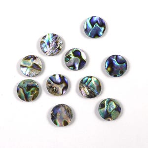 May include: A collection of ten iridescent, round abalone shell beads. The beads display a range of colors, including blues, greens, and purples, with a shimmering, pearlescent effect. They are scattered on a white background.