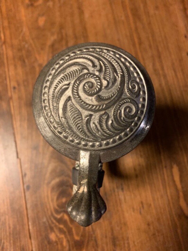 May include: A silver beer stein with a decorative lid featuring a swirling, embossed design. The lid has a small, ornate handle.