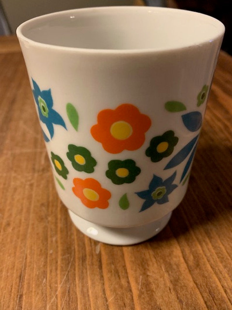 May include: White ceramic mug with a floral design. The flowers are orange, yellow, blue, and green.