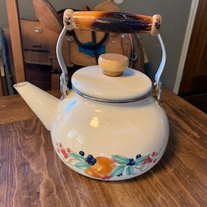 May include: White enamel teapot with a wooden handle and lid. The teapot has a floral design with fruit and berries.