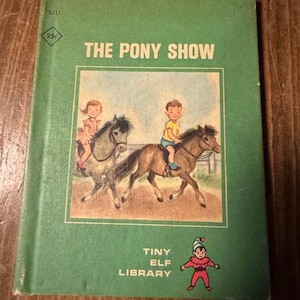 May include: A green book with the title "The Pony Show" on the cover. The cover features an illustration of two children riding ponies. The book is part of the "Tiny Elf Library" series.