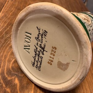 May include: A white ceramic mug with a green and gold design. The bottom of the mug has the text "AVOII Handcrafted in Brazil Exclusively for C.W.P. Products Office, Inc. 1978 5411325"