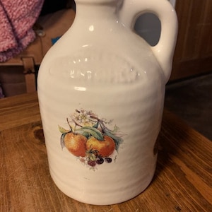 May include: White ceramic pitcher with a handle, featuring a painted design of oranges and berries. The pitcher has a textured surface and the words "Old Fashioned" are embossed on the front.