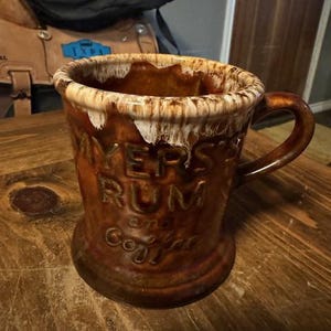 May include: A brown ceramic mug with white glaze and the words "Myers's Rum & Coffee" printed on the side.