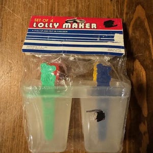以下が含まれることがあります： 緑と青のクマの形をしたハンドルが付いた、透明なプラスチック製のアイスキャンディー型4個セット。パッケージには「Set of 4 Lolly Maker」と「Fill up and put in freezer」と書かれています。