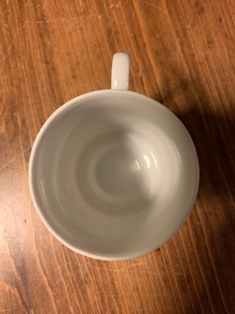 May include: A white ceramic teacup with a simple design. The cup is empty and has a handle on the right side.