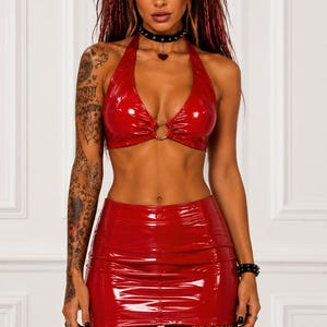 Peut inclure: Un ensemble deux pièces en vinyle rouge brillant composé d'un haut court dos nu avec un anneau métallique central et d'une mini-jupe taille haute assortie. Le haut présente un décolleté en V profond et la jupe a des coutures verticales.