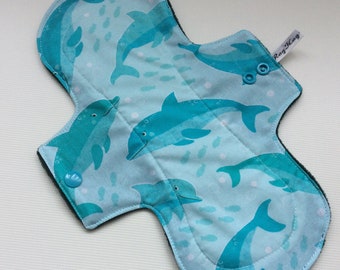 May include: A blue and green reusable cloth pad with a dolphin print and the text "Rag'n'Tag" on the top right corner. The pad has two snaps on the side.
