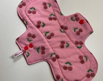 May include: Pink reusable cloth pad with a cherry print and the word "Heavy" on the side. The pad has two red snaps.
