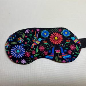 May include: Black sleep mask with a colorful floral and bird pattern. The pattern features hummingbirds, peacocks, and flowers in shades of pink, blue, green, yellow, and red.