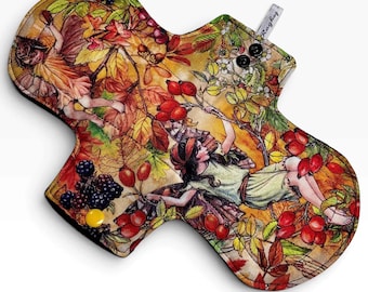 May include: A reusable cloth menstrual pad featuring a colorful autumn-themed print with fairies, red rose hips, and dark blackberries. The pad has a contoured shape, two black snap buttons at the top, one yellow snap button at the bottom, and a small tag.