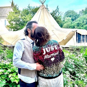 May include: A couple kissing in front of a white teepee tent. The woman is wearing a sequined jacket with the text "JUST Married" on the back.