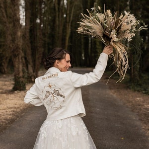 A custom-made ivory leather jacket, designed for the bride's special day. Featuring a pinky promise skeleton couple, this gothic-inspired cover-up symbolizes everlasting love and devotion in a unique, edgy wedding style