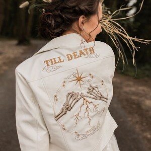 Gothic-inspired ivory bride leather jacket, a bespoke cover-up for the bride. Adorned with a skeleton pinky promise couple, it represents their commitment till death, adding a touch of romance to their wedding ensemble