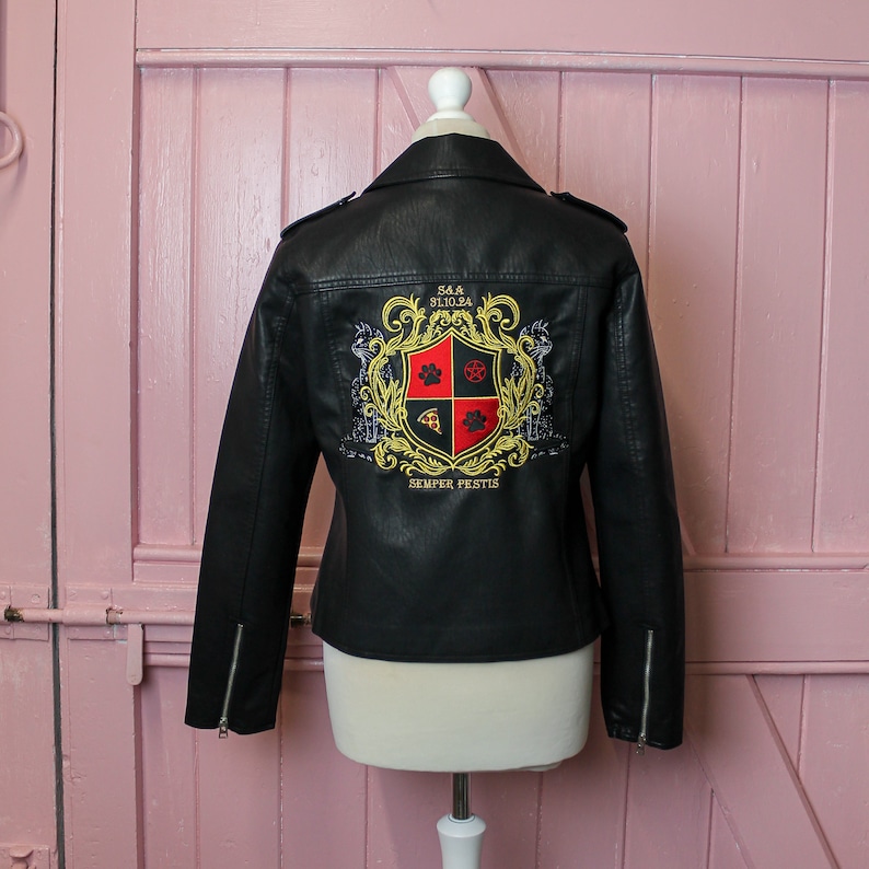 Pu&ograve; includere: Giacca da motociclista nera in ecopelle con stemma ricamato sul retro. Lo stemma presenta un'impronta di zampa, una fetta di pizza e un design a pentagramma. Include dettagli con cerniera e colletto a revers.
