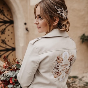 May include: A cream-colored jacket with embroidered floral and text design on the back. The text reads "TOGETHER WE MADE IT". The jacket has a classic collar and shoulder epaulettes. The jacket is part of a wedding theme.