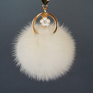 May include: A white fluffy pom-pom keychain with a gold ring and a white flower charm.