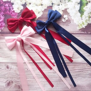 Puede incluir: Tres lazos para el pelo de cinta de satén con colas largas. Los lazos son de color rosa, rojo y azul marino.