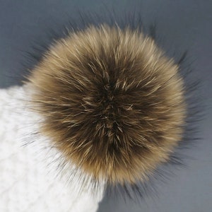 May include: White knitted beanie with a large brown and black faux fur pom pom.