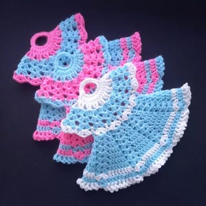 Puede incluir: Tres paños de cocina de ganchillo en forma de vestidos. Uno es azul claro con ribete blanco, otro es de rayas rosa y azul, y el último es de rayas rosa y azul con ribete blanco.