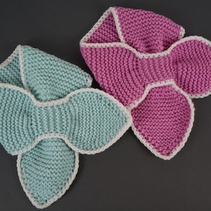 May include: Two knitted neck warmers, one in light blue and one in pink, with white trim. The neck warmers are shaped like a bow.