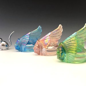 May include: A chrome cat figurine with a raised tail sits next to three iridescent glass sculptures. The sculptures depict Native American chiefs with feathered headdresses in blue, pink, and green hues. The glass has a shimmering, opalescent finish.