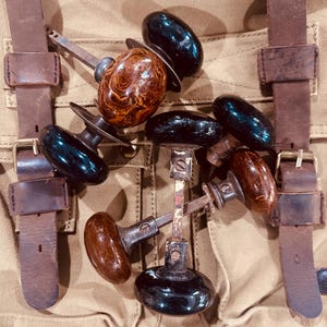May include: A collection of vintage door knobs featuring a mix of solid black and marbled brown finishes. The knobs are round with metal spindles and mounting hardware attached, showcasing various textures and glossy surfaces in a group arrangement.