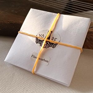 May include: A white envelope with a rubber band around it. The envelope has a sticker on it that says "Fluocarbon" and a logo with the word "YORE".