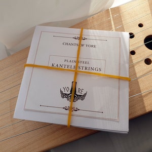 Peut inclure: Un paquet de cordes en acier brut pour un kantele, un instrument à cordes finlandais. Le paquet est étiqueté "Chants of Yore" et "Plain Steel Kantele Strings".